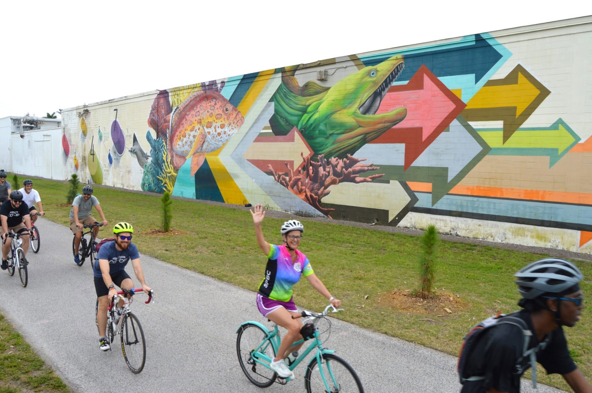 a group of people bike next to a big mural